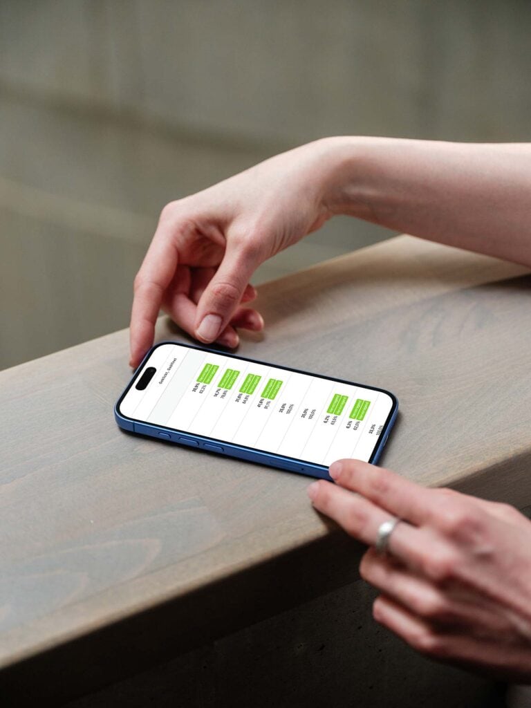 mockuuups iphone 16 mockup on a wooden surface with a hand interacting scaled